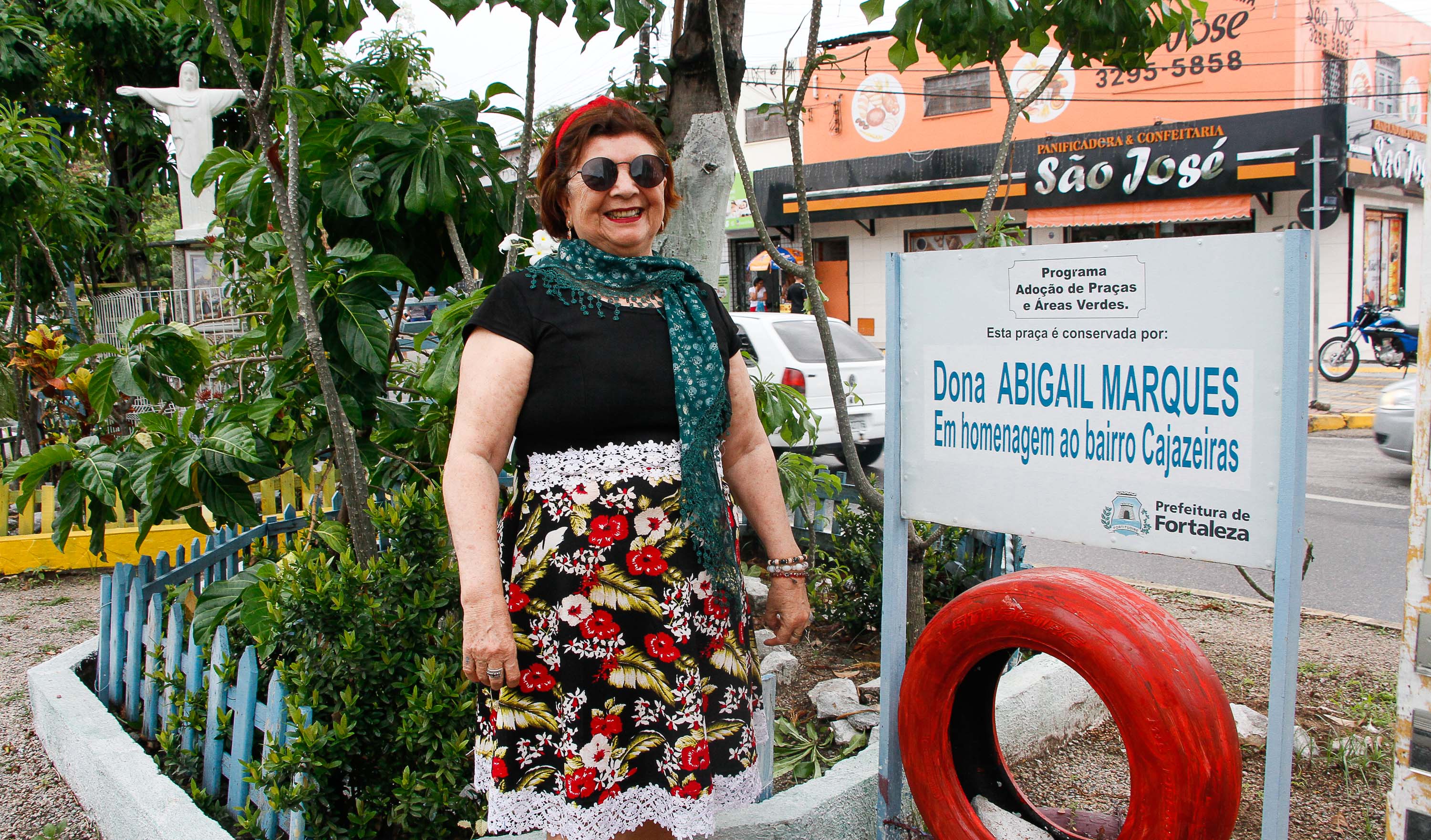 senhora posa em frente ao canteiro de plantas do qual toma conta